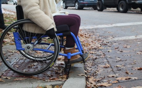 student in wheelchair struggling to go over bump in sidewalk